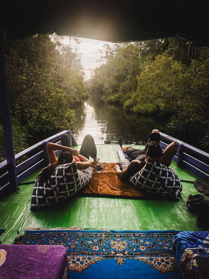 ruta por indonesia atardecer en klotok, dos personas tumbadas con cojines en el suelo de un barco de madera